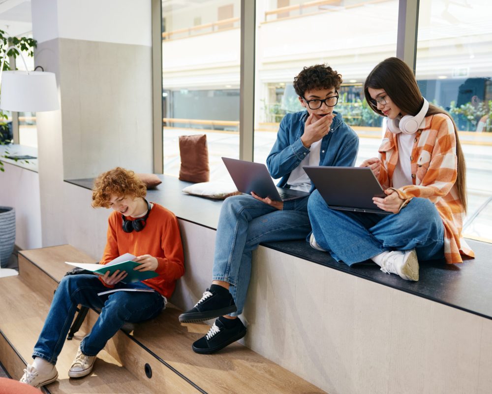 Group of teenagers in coworking office making money online. Young workers with laptops and papers discussing strategy